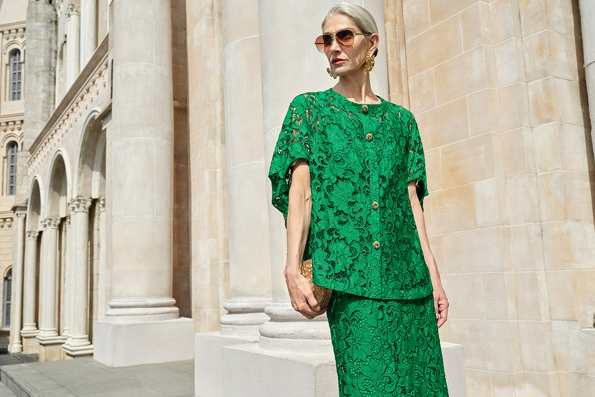 Elegant older woman in a bright green lace skirt set standing outside a grand stone building