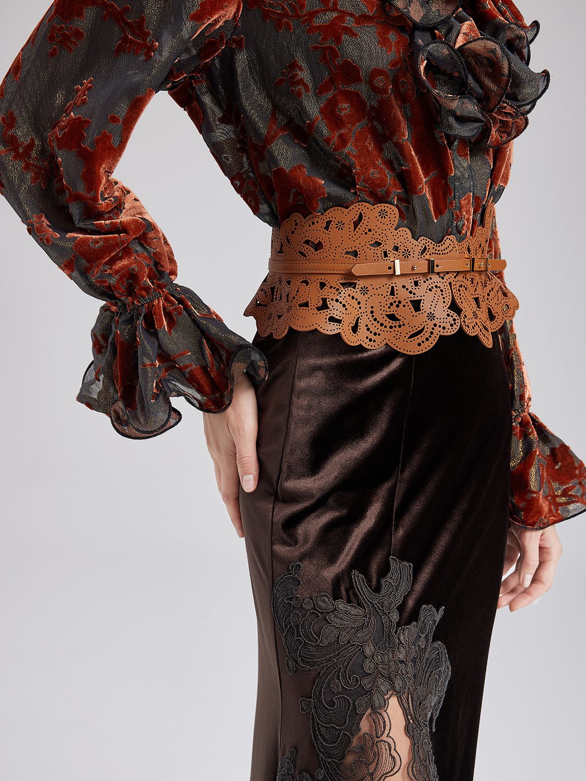 Close-up of a woman wearing a floral velvet blouse, brown lace belt, and black satin skirt with lace appliqué