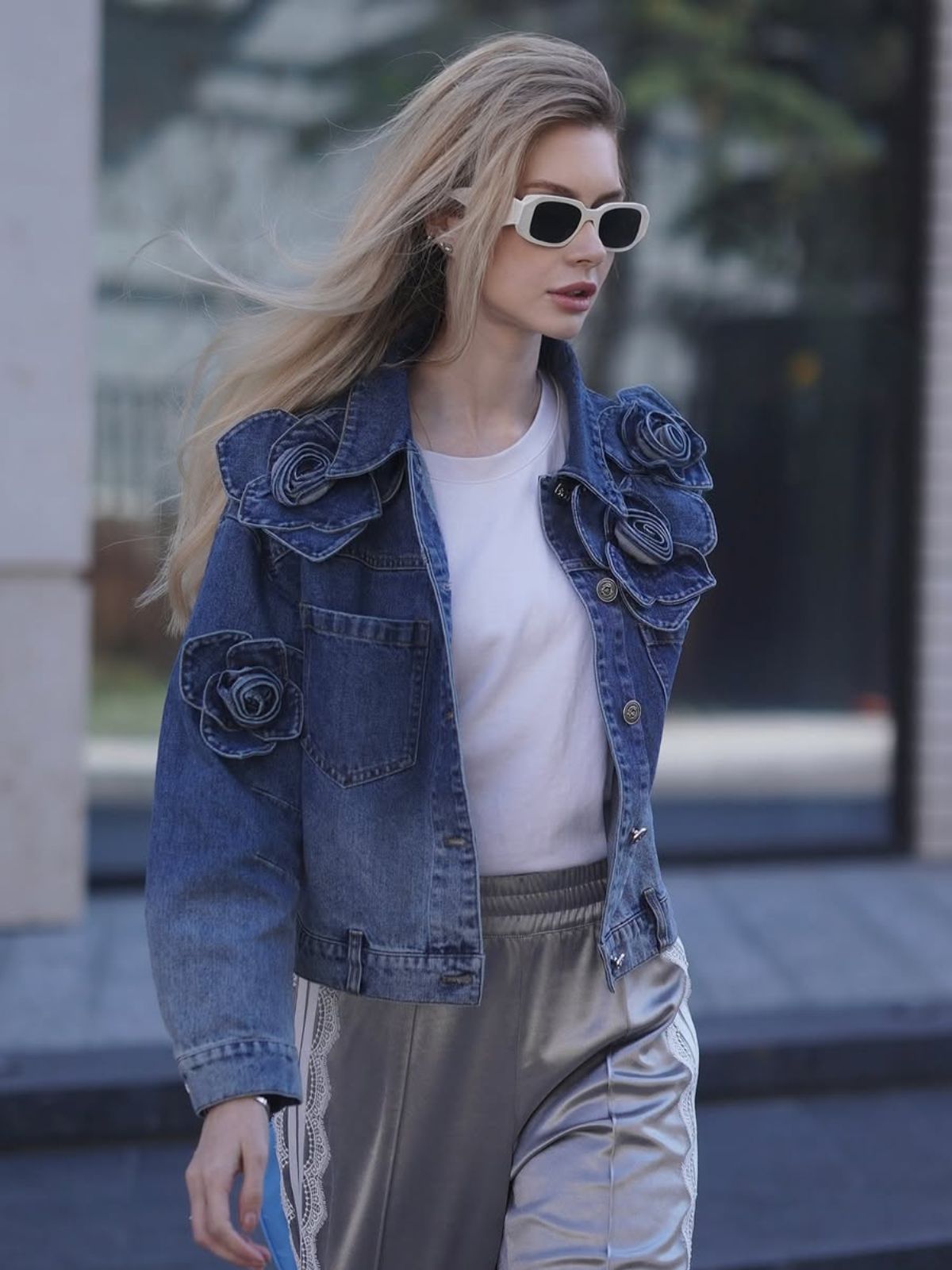 Woman wearing a blue floral-appliqué denim jacket and white sunglasses