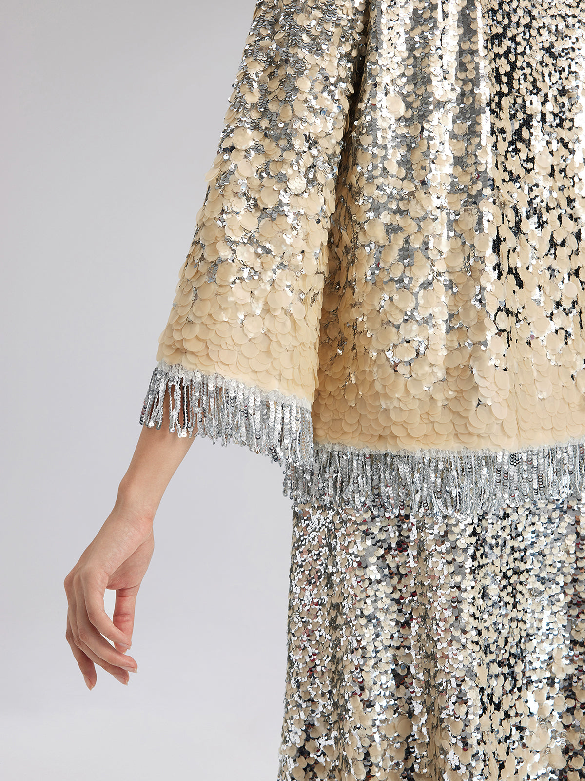 Detailed close-up of a champagne sequin jacket featuring textured embellishments and silver fringe trim