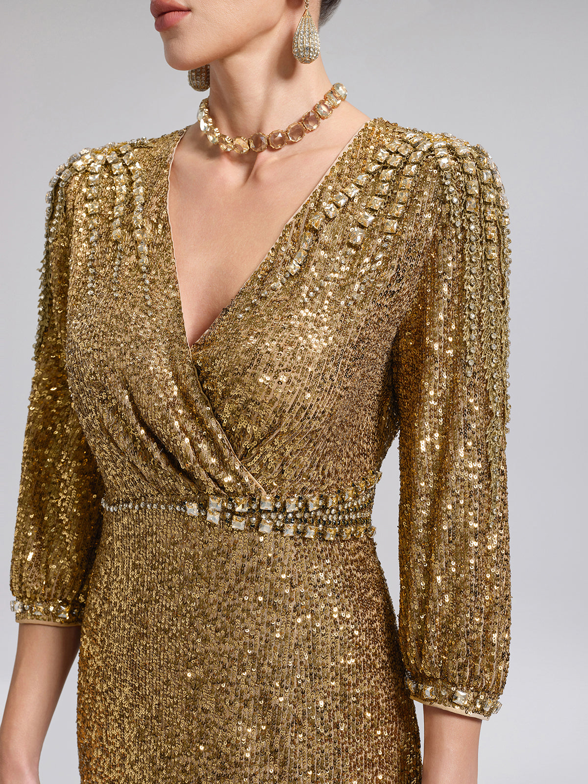 Detailed close-up of a gold sequin evening dress featuring a V-neckline, shimmering fabric, and decorative waist embellishment