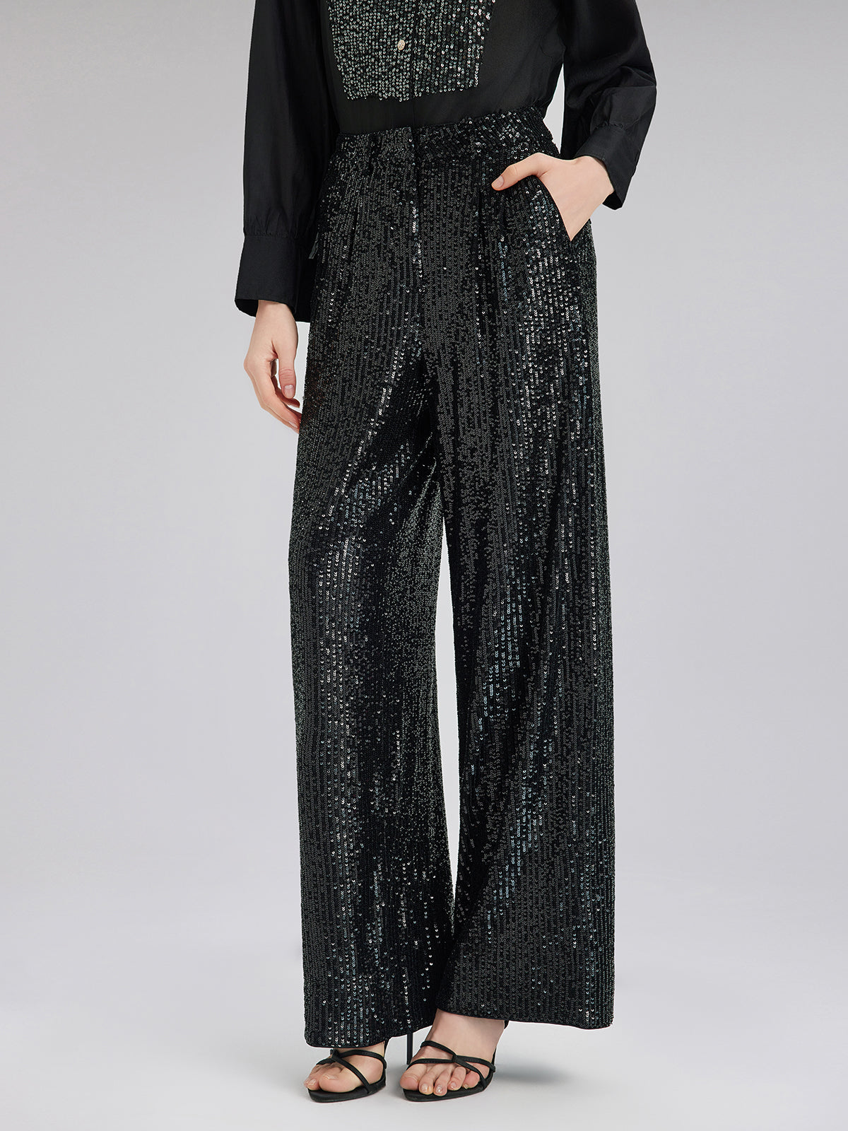 Woman wearing a black sequin wide-leg jumpsuit with long sleeves and sparkling details