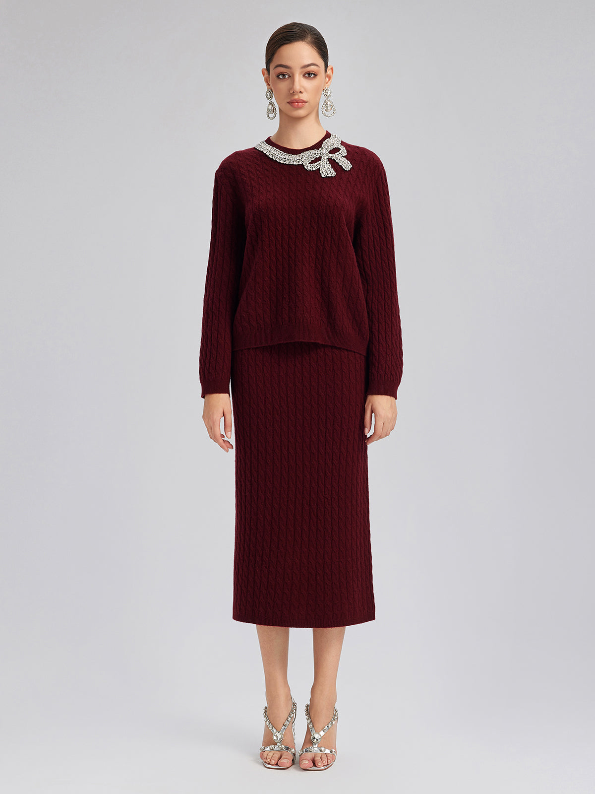 Elegant woman in a burgundy textured knit sweater and matching midi skirt featuring a jeweled bow neckline