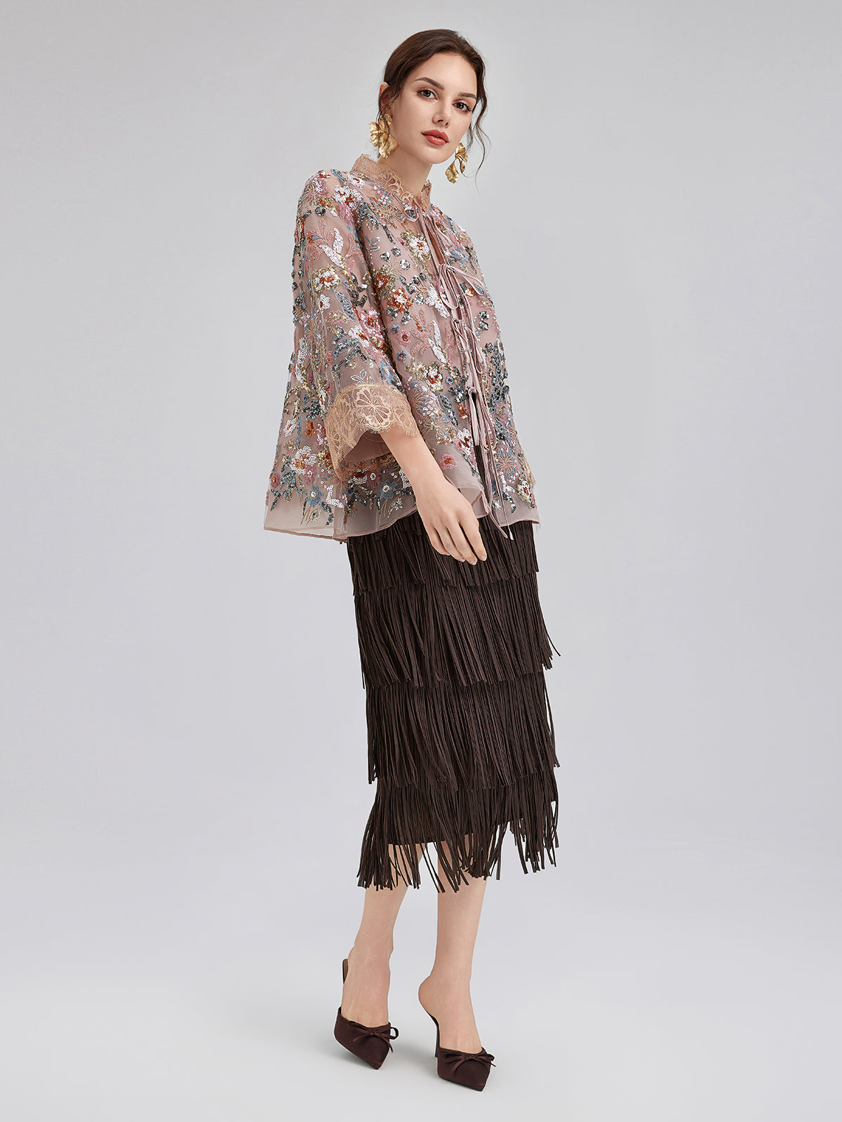 Elegant woman in a pink floral embroidered sheer jacket paired with a layered black fringe skirt