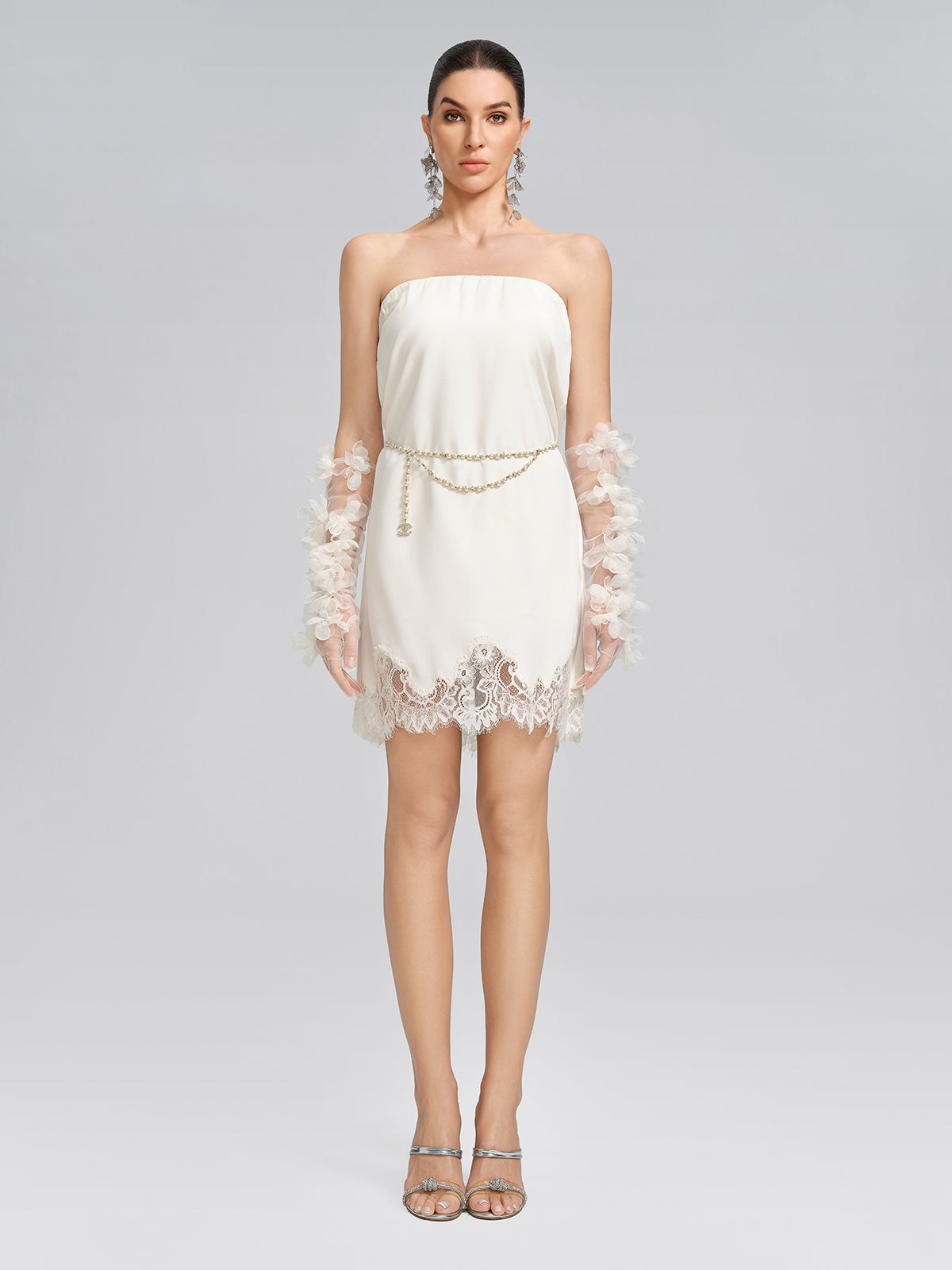 Elegant woman in a white strapless dress featuring delicate lace trim, floral sleeve embellishments, and a refined silhouette