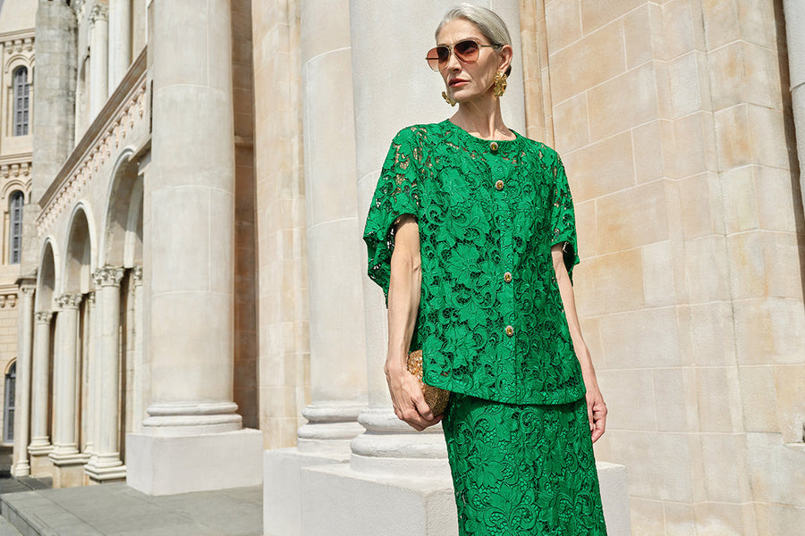 Elegant older woman in a bright green lace skirt set standing outside a grand stone building