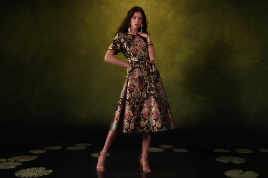 Woman wearing a black and gold floral brocade midi dress with a belted waist and flared skirt