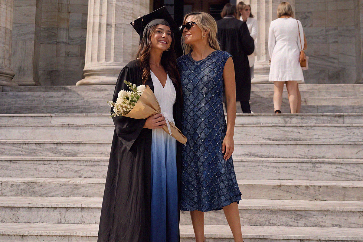 Mother in a navy midi dress posing with her daughter in a graduation gown