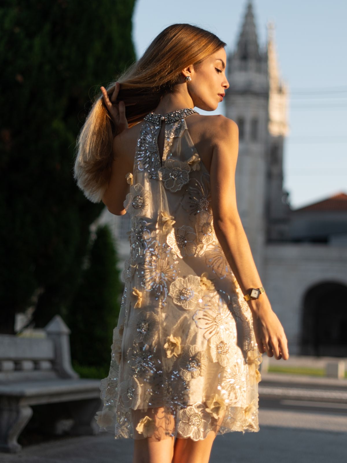 Elegant woman in a white sheer embroidered mini dress with floral appliqué details in an outdoor setting