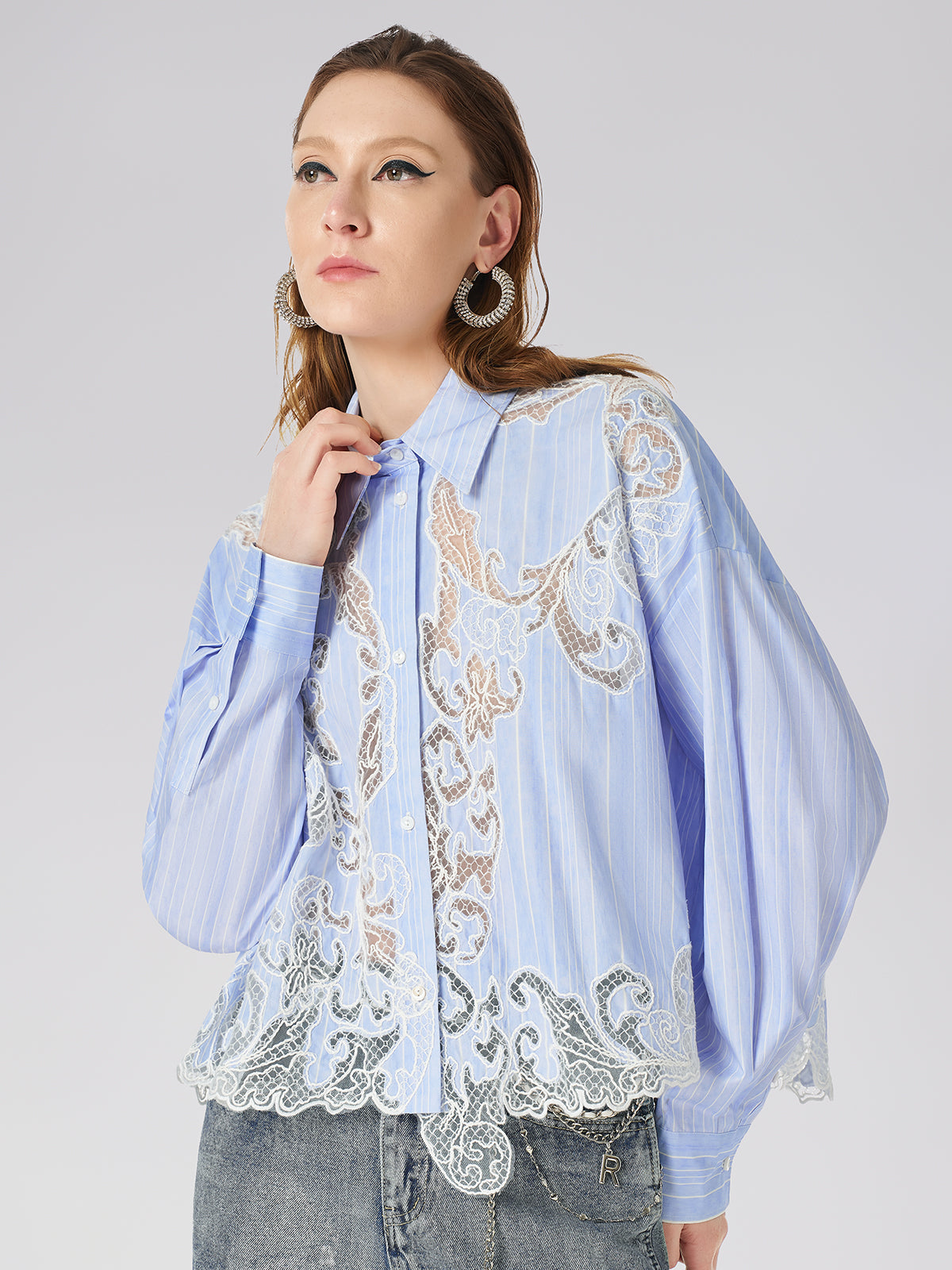 Elegant woman in a light blue striped shirt with intricate white lace embroidery and long sleeves