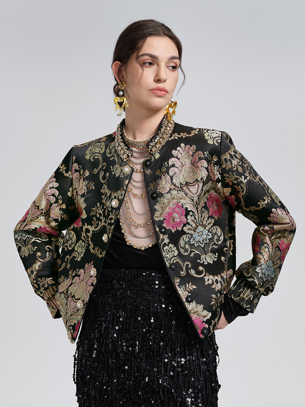 Elegant woman in a black embroidered floral jacket featuring metallic patterns and a sparkling sequin skirt