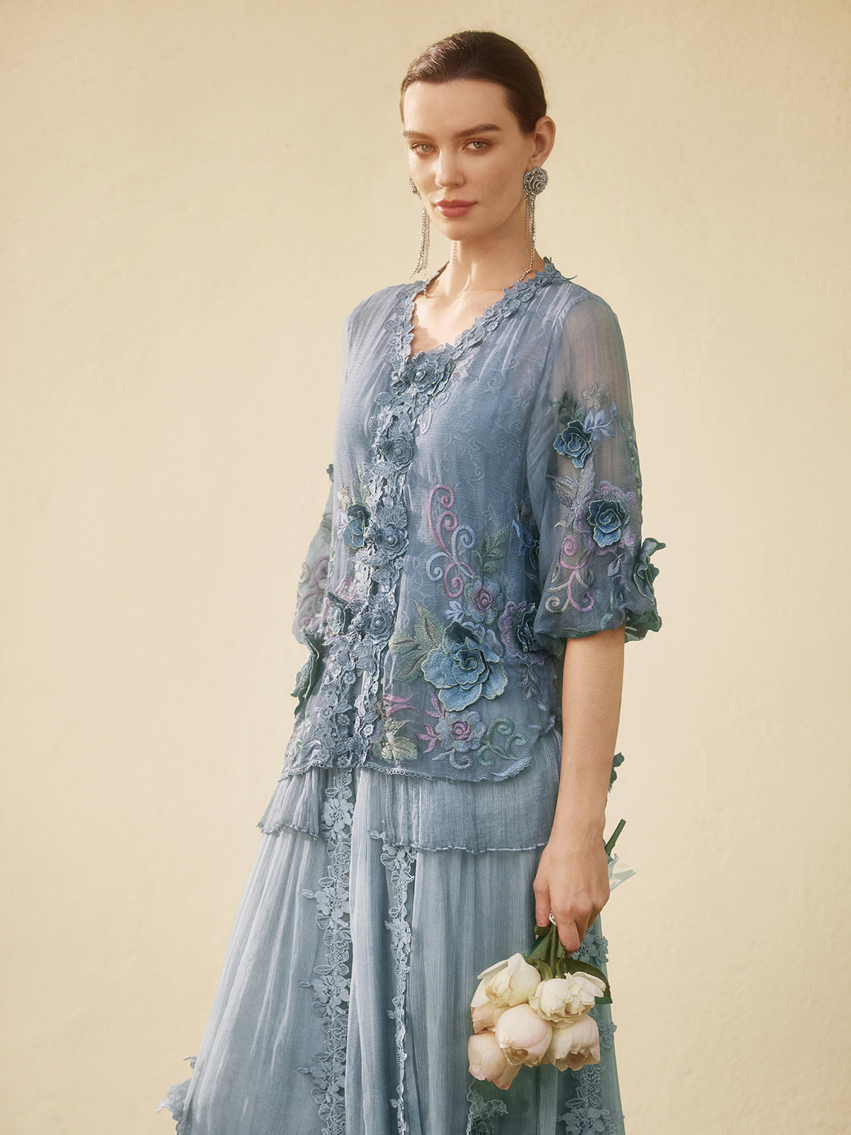 Elegant woman in a light blue embroidered jacket and layered skirt with floral details