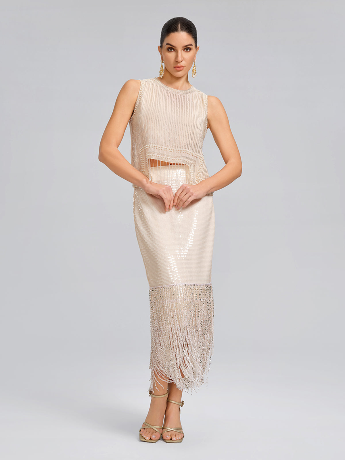Elegant woman in a white sleeveless evening dress featuring shimmering sequins, waist cutout design, and fringe hem detailing