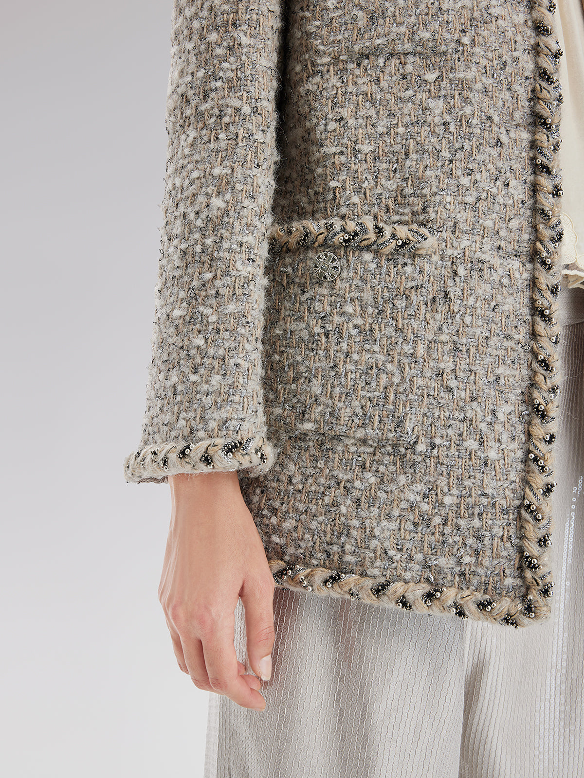 Detailed close-up of a beige tweed jacket featuring textured fabric and decorative edge detailing